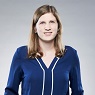 Lächelnde junge Frau mit langen blonden Haaren und einem blauen Oberteil.