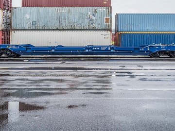 Blauer Intermodalwaggon vor mehreren gestapelten Containern