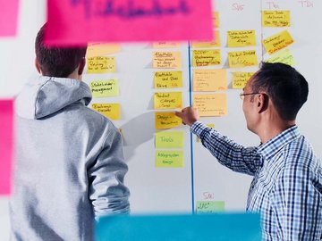 Zwei Mitarbeiter kleben Post-its an ein Whiteboard