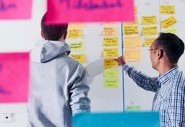 Zwei Mitarbeiter kleben Post-its an ein Whiteboard 