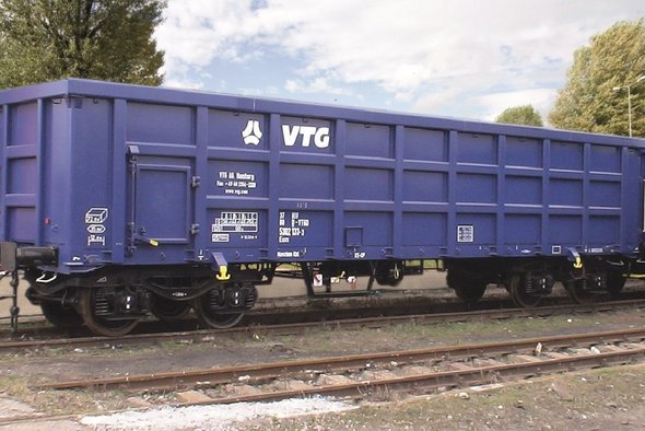 Blauer Boxwagen auf einem Gleis vor grünen Bäumen.