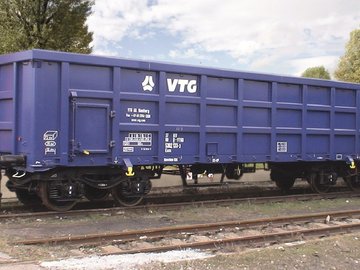 Blauer Boxwagen auf einem Gleis vor grünen Bäumen.