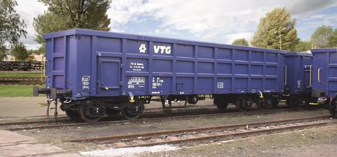 Blauer Boxwagen auf einem Gleis vor grünen Bäumen.