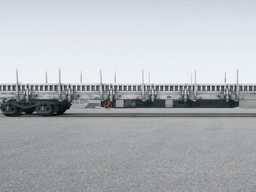 Grauer metallischer Flachwagen mit seitlichen Elementen auf grauem Untergrund.
