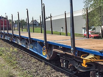 Blauer Flachwagen mit seitlichen Elementen vor einer grauen Halle.