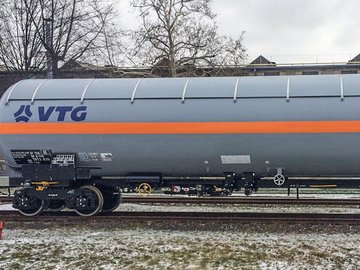 Grauer Flüssiggas-Kesselwagen mit orangem Streifen und blauem Logo auf einer Schiene.