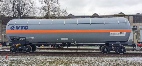 Grauer Flüssiggas-Kesselwagen mit orangem Streifen und blauem Logo auf einer Schiene.