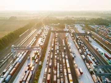 Luftaufnahme eines Güterbahnhofs mit Containern und Gleisen bei Sonnenaufgang