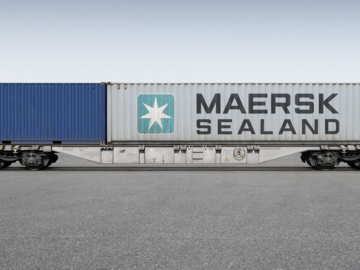Grauer Containerwagen mit einem kleinen blauen Container und einem großen grauen Container darauf.