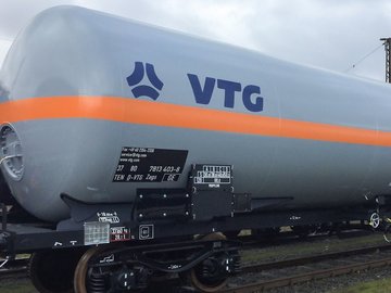 Grauer Flüssiggas-Kesselwagen mit orangem Streifen und blauem VTG-Logo.